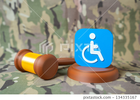 Judge's gavel and symbol of people with disabilities on military background. Assignment of disability status to seriously wounded personnel. Benefits and compensation for veterans and injured soldiers 134335167