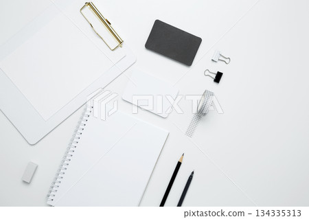 Monochrome stationery items. On a white background, an empty mock up notebook and clipboard, white and black cards Monochrome stationery items. On a white background, an empty mock up notebook and clipboard, white and black cards 134335313