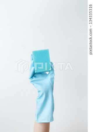 Hand in blue rubber glove holding a sponge for cleaning. Household cleaning and hygiene concept Hand in blue rubber glove holding a sponge for cleaning. Household cleaning and hygiene concept 134335316
