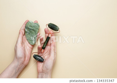 Female hands holding marble face roller and gua sha tools for skincare routine 134335347