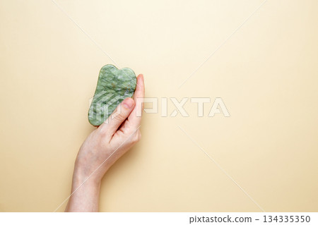 Female hand holding marble gua sha tools for skincare routine 134335350