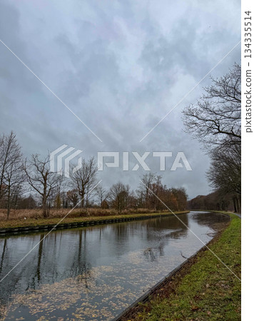 Serene Canal Reflecting Overcast Sky With Sparse Trees And Subtle Ripples Creating Contemplative Serene Canal Reflecting Overcast Sky With Sparse Trees And Subtle Ripples Creating Contemplative 134335514