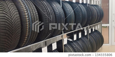 New automotive tires are neatly stacked on metal shelving in a tire shop or auto parts store, displaying various tread patterns and price tags 134335806