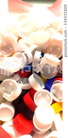 A close-up shot from above of a large pile of assorted plastic bottle caps, mostly white, with splashes of blue, yellow and red, suggesting recycling or sorting A close-up shot from above of a large pile of assorted plastic bottle caps, mostly white, with splashes of blue, yellow and red, suggesting recycling or sorting 134335809