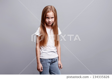 Moody angry young girl staring from under her brow, expressing hurt feelings, negative emotions while standing in studio, kids emotional portrait and facial expression on neutral background 134335826