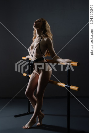 Sensual woman posing in lingerie against a dark background with ballet barre 134335845
