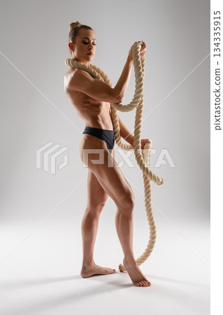 Fitness model displays strength and grace with ropes in a studio 134335915