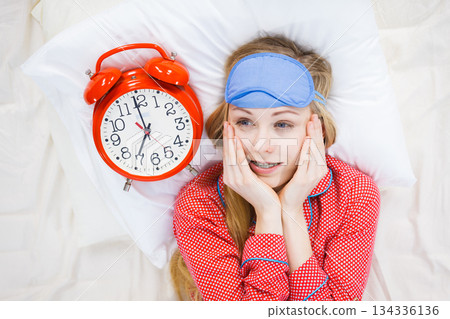 Shocked woman wearing pajamas holding clock overslept 134336136