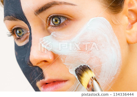 Girl black mask on half face apply white mud Girl black mask on half face apply white mud 134336444