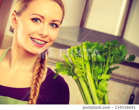 Woman in kitchen holds green celery 134336691