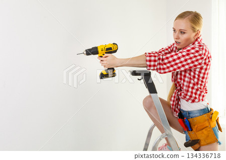 Woman using drill on ladder Woman using drill on ladder 134336718