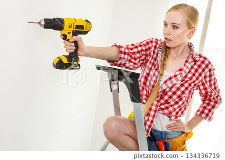 Woman using drill on ladder 134336719