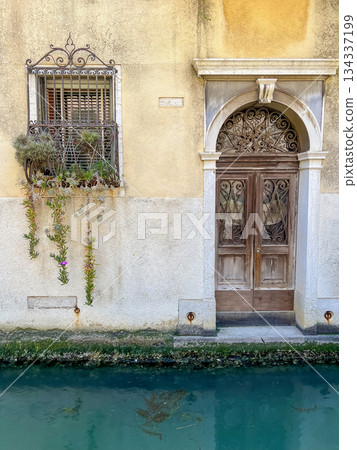 A rustic wooden door with intricate carvings stands beside a canal in Venice 134337199