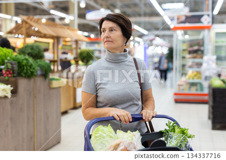 Mature woman standing in grocery store with groceries in cart 134337716