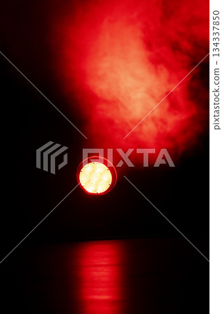 Red lights shine through thick smoke in a dark room during a performance 134337850