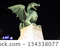 A stone dragon statue standing on the railing of the Dragon Bridge in the center of Ljubljana, the capital of Slovenia 134338077