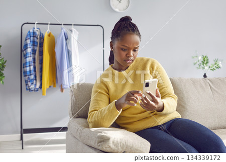 Woman sitting on sofa at home and using mobile phone for text messaging or online shopping Woman sitting on sofa at home and using mobile phone for text messaging or online shopping 134339172
