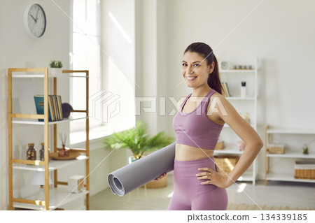Happy slim sporty woman going to do sport exercises holding yoga mat in hands at home. Happy slim sporty woman going to do sport exercises holding yoga mat in hands at home. 134339185