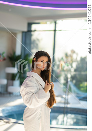 Woman in white bath robe standing near the pool in a spa center 134341031