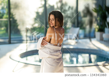 Woman in white bath robe standing near the pool in a spa center 134341060