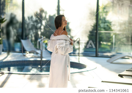 Woman in white bath robe standing near the pool in a spa center 134341061