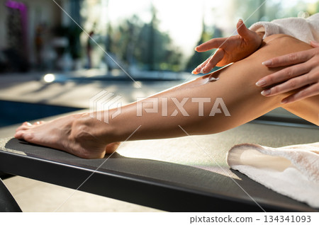 Close up of woman sitting on a beach chair and applying cream on her legs 134341093