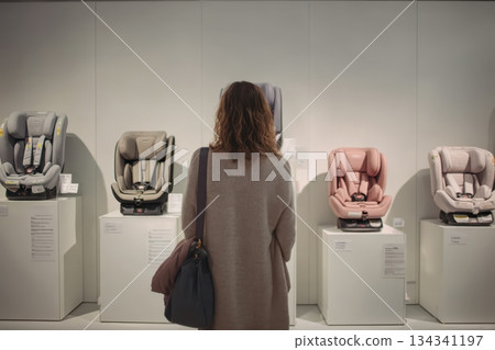 Woman standing against safety car seats for kid. Shelf with child car seats. Car seats displayed on shelves showcasing safety and modern design for Children. Baby shop. Newborn expecting concept 134341197