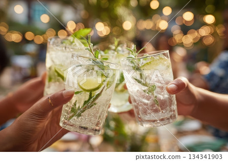 Friends drinking sparkling cocktails. People clinking glasses with drinks outdoors. Close up of hands cheers, making toasts and touch with wineglasses at garden party. Warm Summer Evening. Enjoy Life 134341903