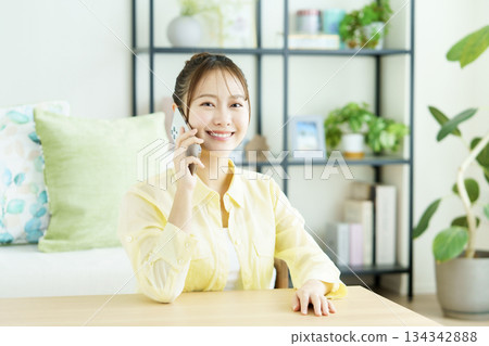 一位微笑的日本女性在客廳裡用智慧型手機通話的肖像 一位微笑的日本女性在客廳裡用智慧型手機通話的肖像 134342888