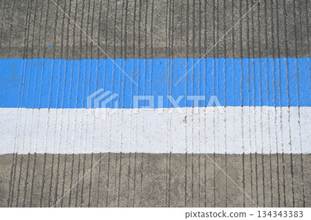 A close-up photograph of a concrete road surface featuring a vertical ridged texture.Blue and white strip are painted on the concrete road. 134343383