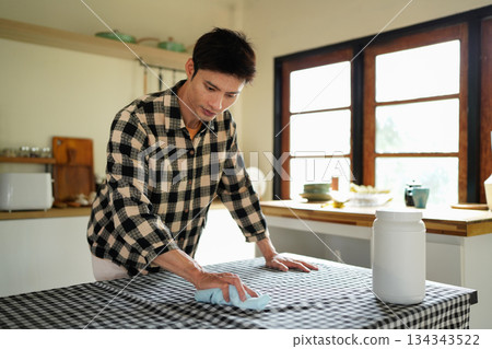A man wiping a table with a cloth in a home kitchen, keeping the area clean 134343522