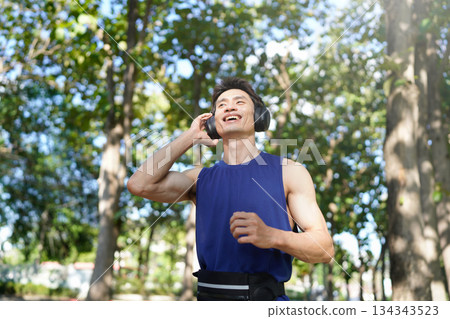 A man jogging outdoors while listening to music with headphones, smiling and enjoying 134343523