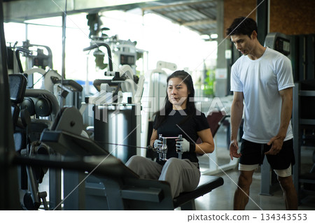 Trainer supervising woman during seated row workout Trainer supervising woman during seated row workout 134343553