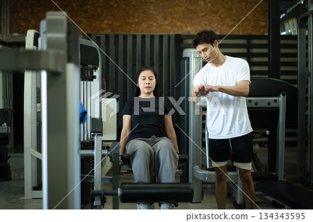 Trainer teaching leg extension exercise at gym Trainer teaching leg extension exercise at gym 134343595