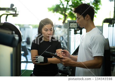 Trainer reviewing workout plan with woman at gym Trainer reviewing workout plan with woman at gym 134343598