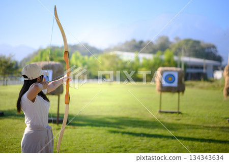 Woman practicing archery at straw targets outdoors Woman practicing archery at straw targets outdoors 134343634