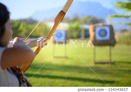 Woman practicing archery at straw targets outdoors Woman practicing archery at straw targets outdoors 134343637