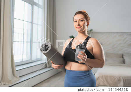 Yoga fitness sport workout training. Woman hold yoga mat bottle water ready for practicing yoga at home. Plus size female doing sports indoor. Girl in sportswear have training workout for weight loss 134344218