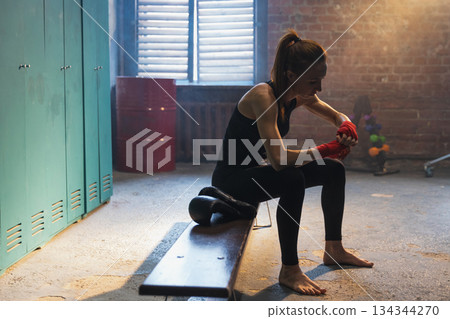 Women self defense girl power. Woman fighter preparing for fight wrapping hands with red boxing wraps sports protective bandages. Strong girl ready for fight active exercise sparring workout training 134344270