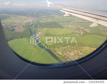 Airplane window view wing over river and green fields rural landscape 134344305