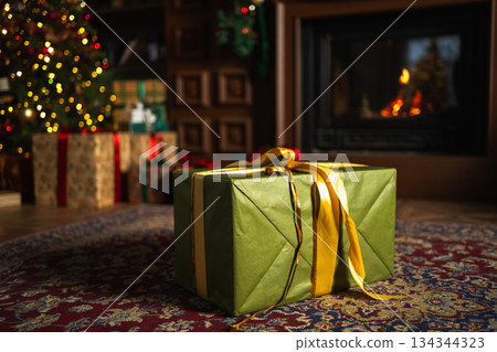 Green gift box in classical Christmas decorated interior living room library with fireplace. Christmas gift near fir tree on Christmas eve. Modern classic style interior design apartment. Christmas Green gift box in classical Christmas decorated interior living room library with fireplace. Christmas gift near fir tree on Christmas eve. Modern classic style interior design apartment. Christmas 134344323