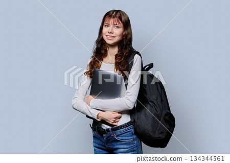 Portrait of beautiful girl teenage student with backpack, laptop on gray background Portrait of beautiful girl teenage student with backpack, laptop on gray background 134344561