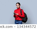 Portrait of beautiful female teenage student with backpack, smartphone on gray background 134344572