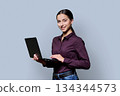 Portrait of smiling young woman holding laptop on gray studio background 134344573