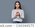 Portrait of serious teenage girl holding smartphone on gray studio background 134344575