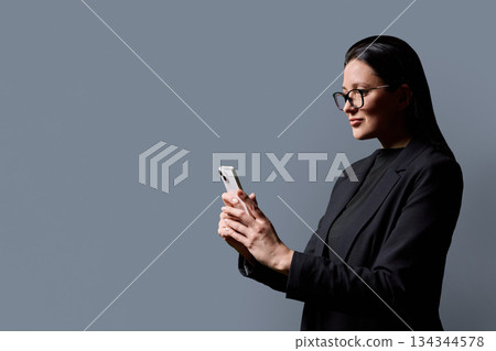 Profile portrait of successful middle-aged businesswoman with smartphone on grey background Profile portrait of successful middle-aged businesswoman with smartphone on grey background 134344578
