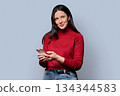 Beautiful smiling woman holding smartphone, on gray studio background 134344583