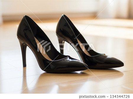 Black shiny high heels resting on a wooden floor bathed in bright natural light 134344726