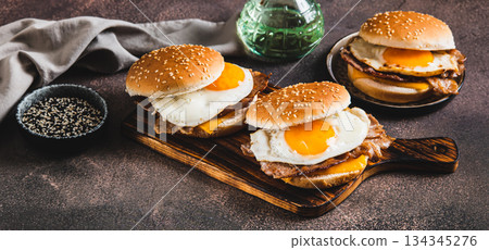 Burgers with fried egg, bacon and cheese on a board on a table web banner 134345276