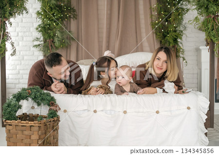 A little sister kisses her younger brother lying on the bed next to parents. Christmas family morning. 134345856
